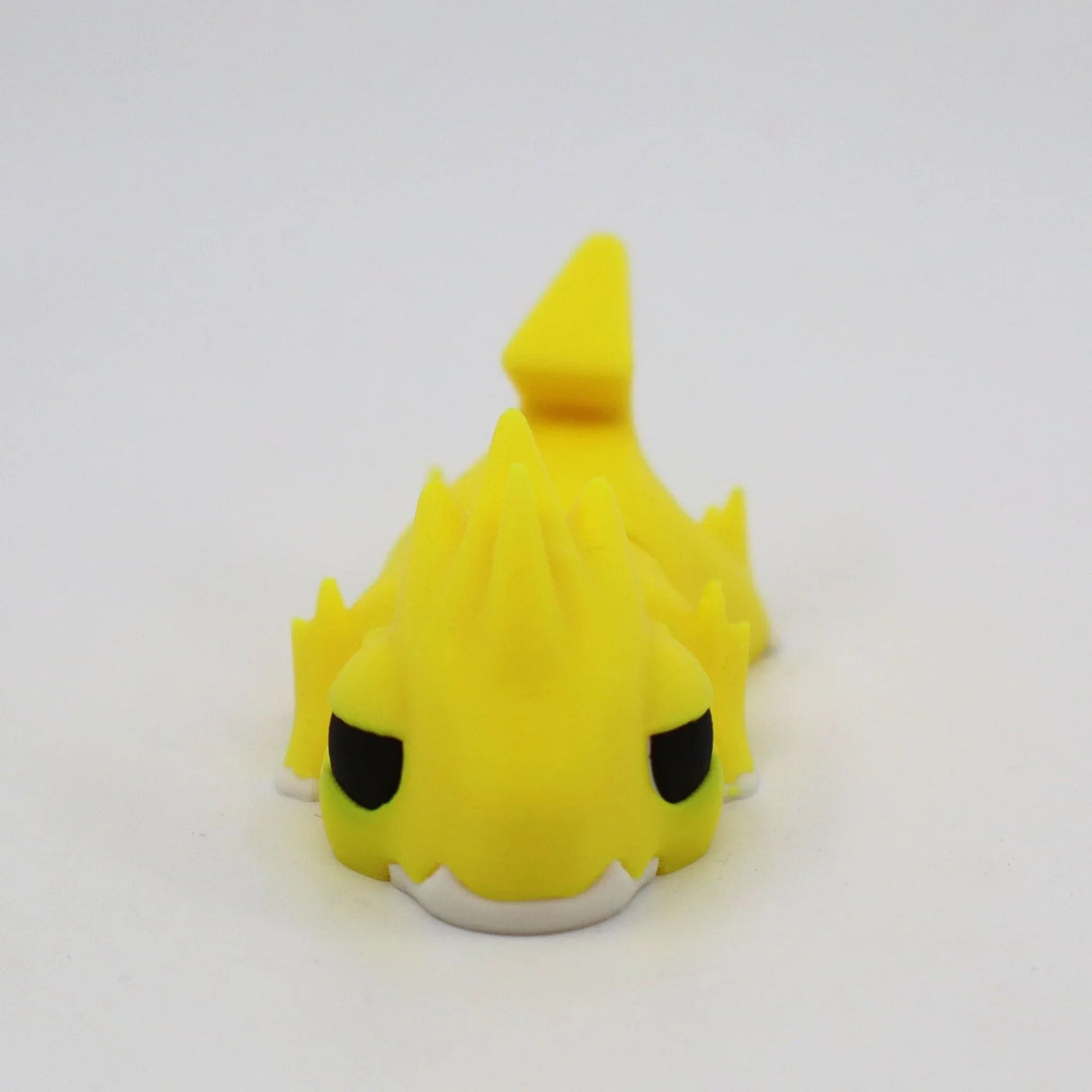 Yellow 3D printed sensory toy dragon with spikes and black eyes on a white background.