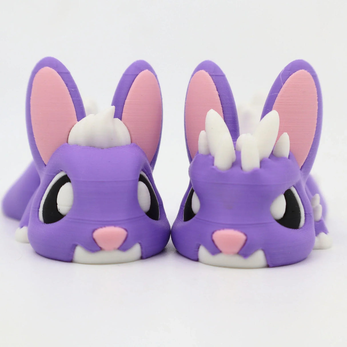 Pair of purple 3D printed sensory bunny toys with big eyes and pink ears on white background
