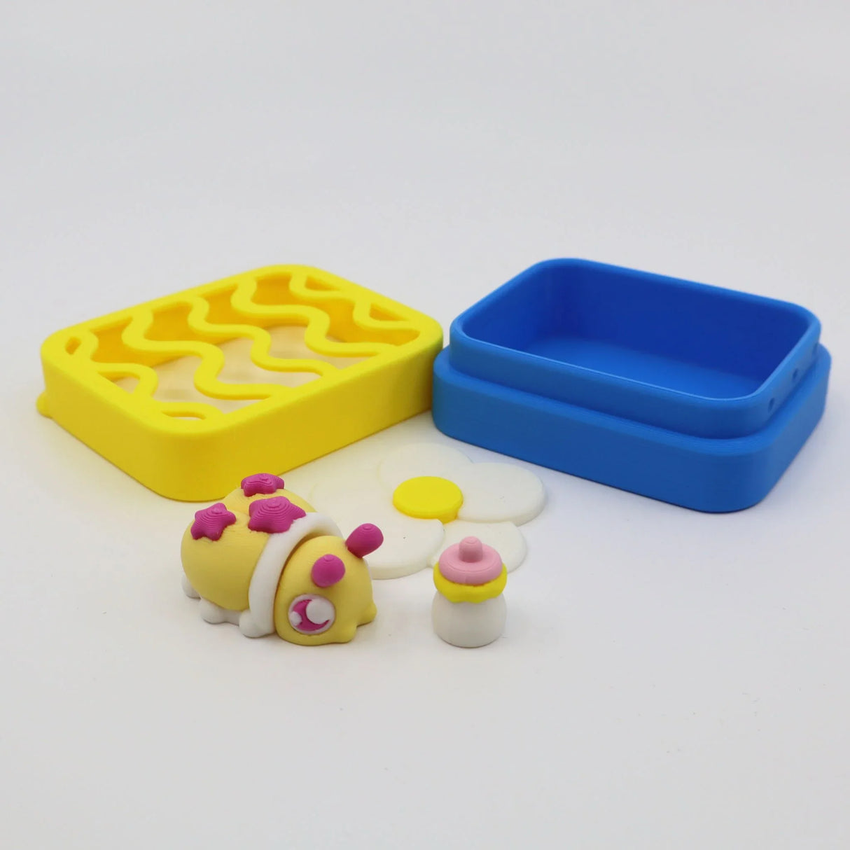 Colorful 3D printed sensory toy set with bee, flower, bottle, yellow tray, and blue box