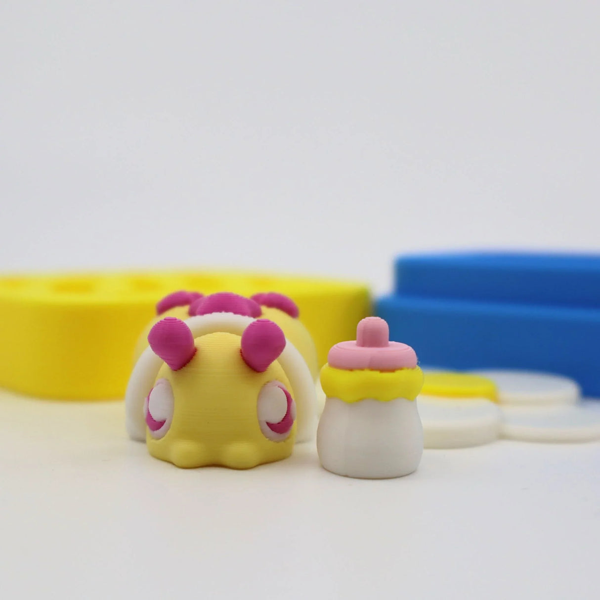 Colorful 3D printed sensory toy bug with baby bottle, yellow and blue shapes in background