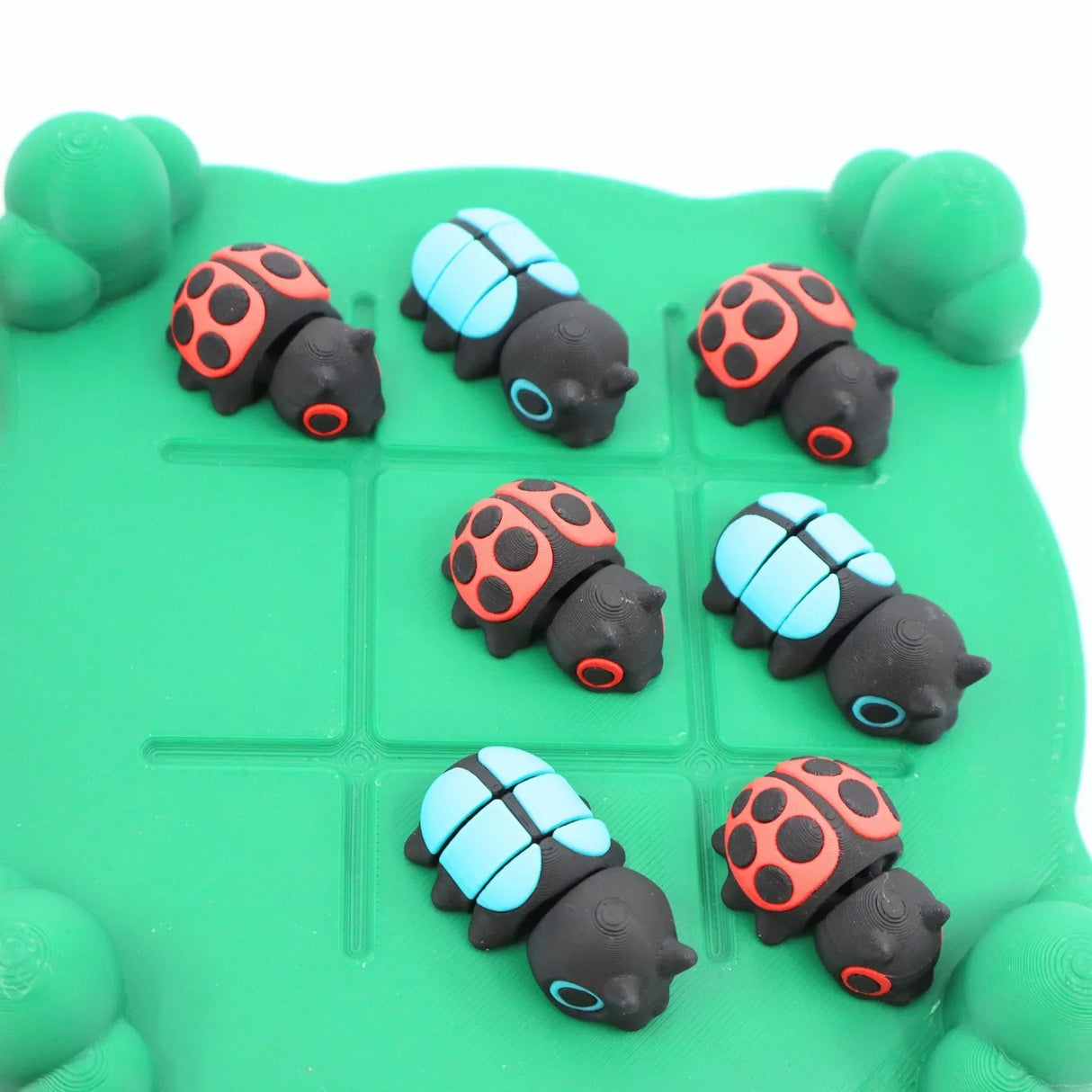 Colorful 3D printed ladybug and beetle sensory toys on green grid for tactile play
