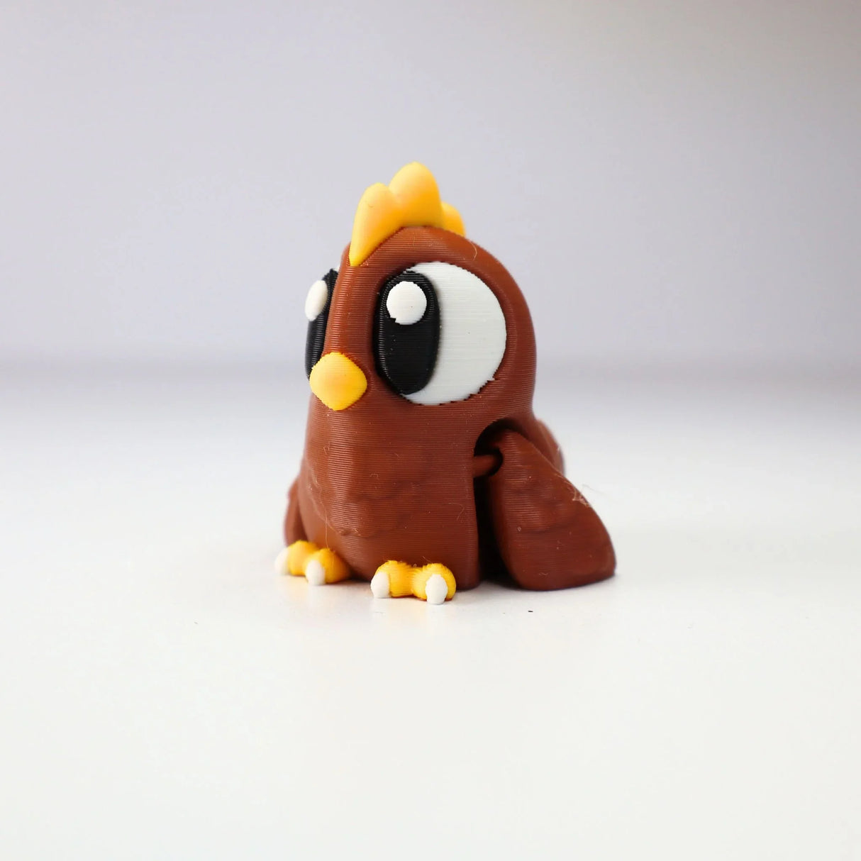 Cute 3D printed brown chicken sensory toy with large eyes, yellow beak, and white background.