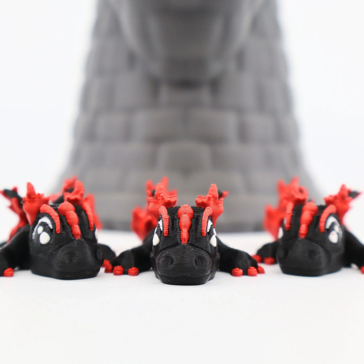 Three small black and red 3D printed dragon sensory toys in front of a gray castle tower.
