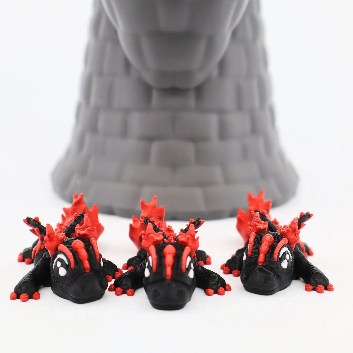 Three black and red 3D printed dragon toys in front of a grey castle tower