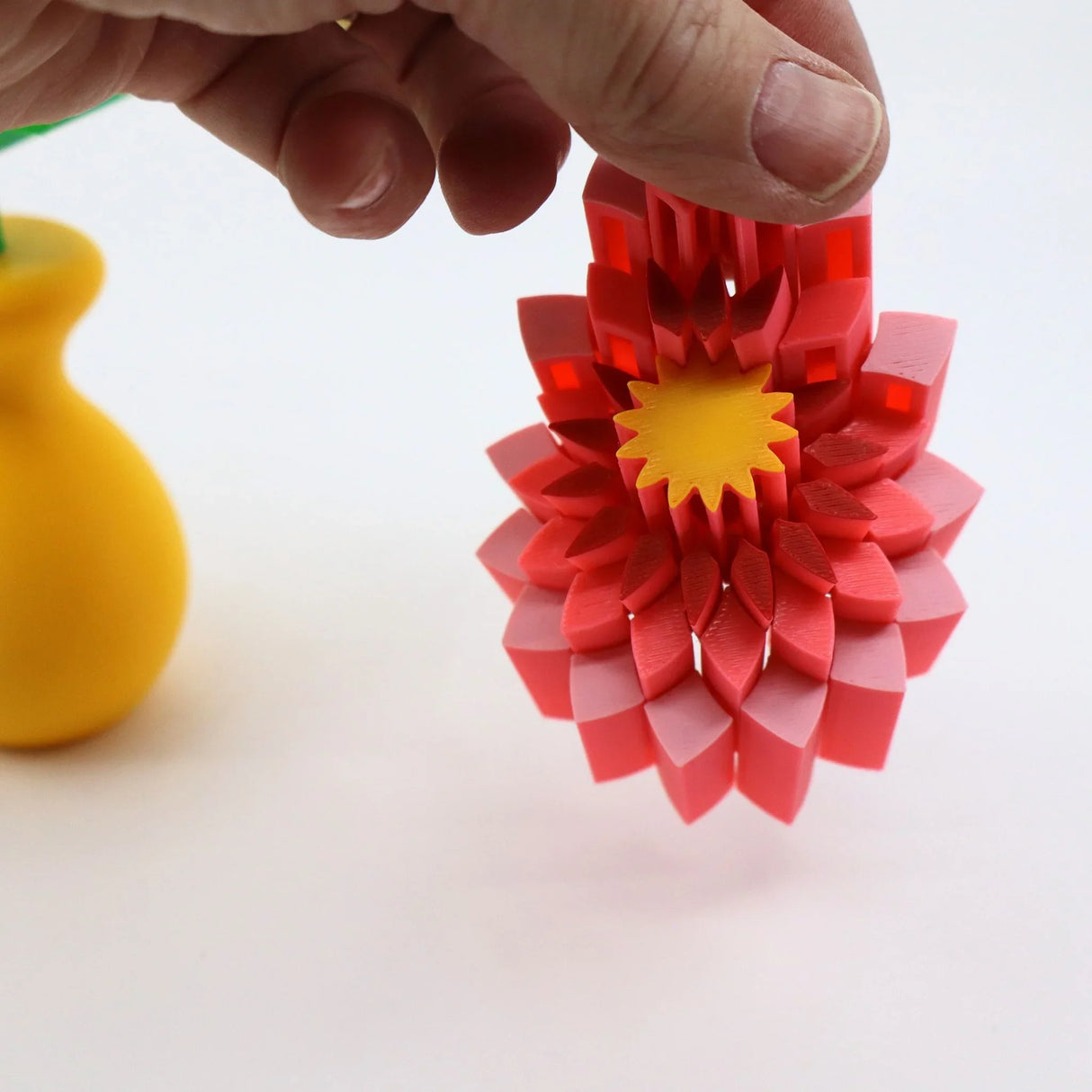 Hand holding a colorful 3D printed sensory flower toy with pink petals and yellow center