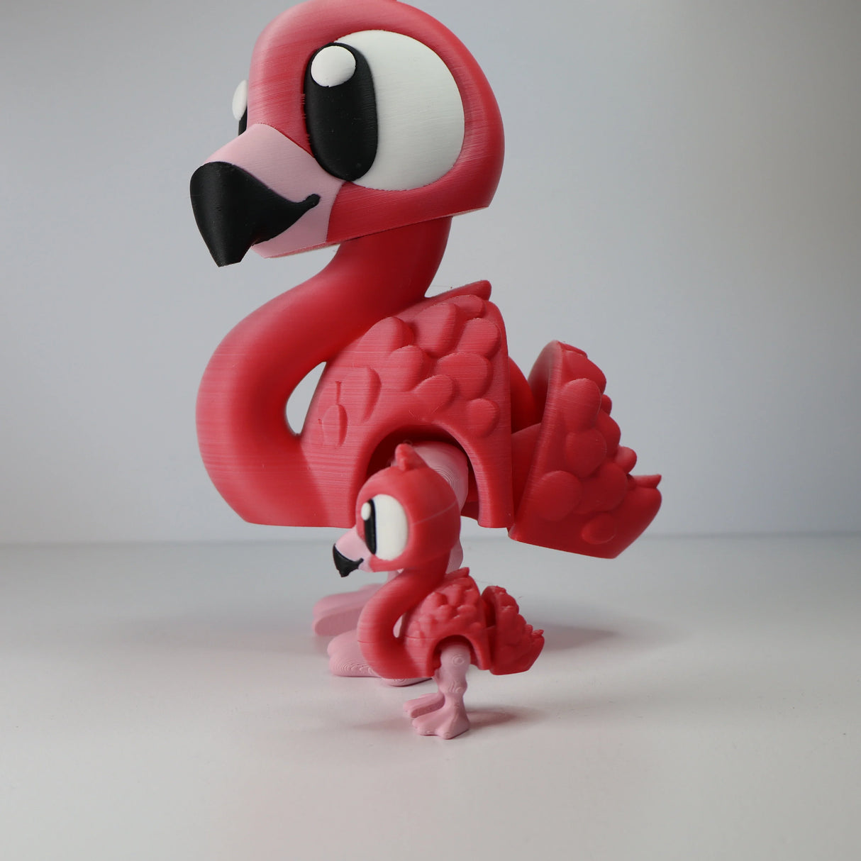Two pink 3D printed flamingo sensory toys with movable wings and cartoon eyes