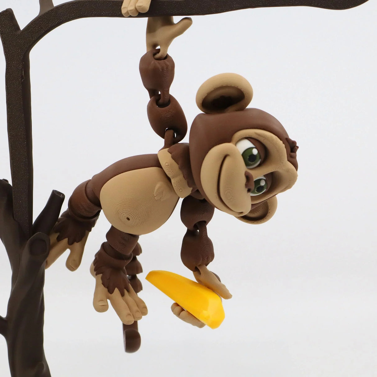 3D printed sensory monkey toy hanging from a tree and holding a yellow banana