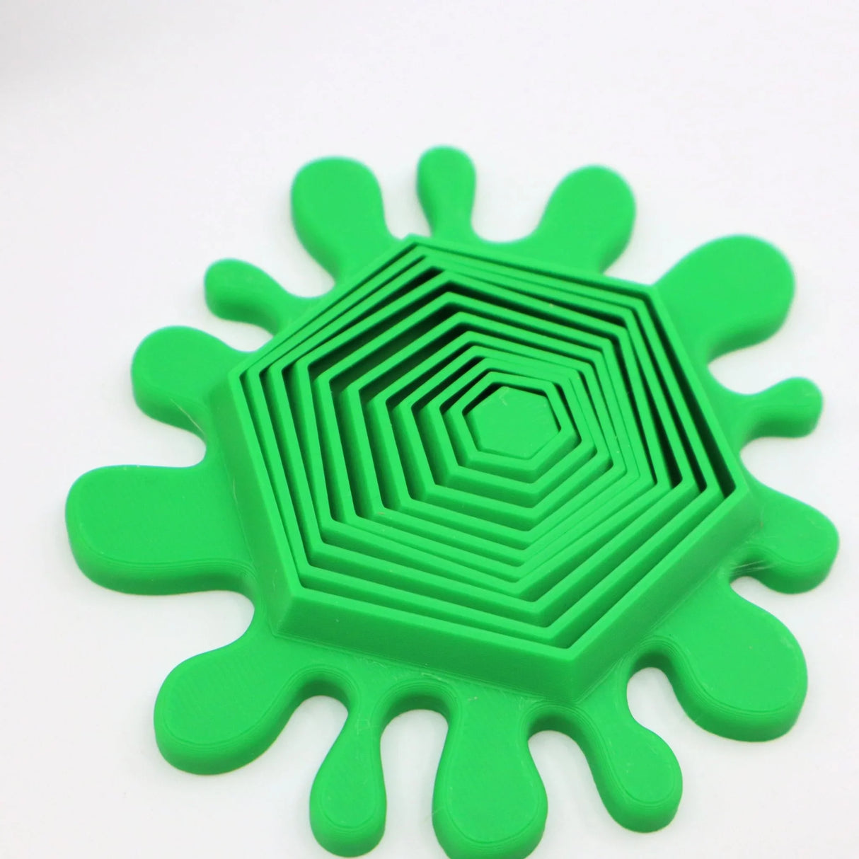 Green 3D printed sensory toy with hexagonal stacking pieces and splatter edges on white background