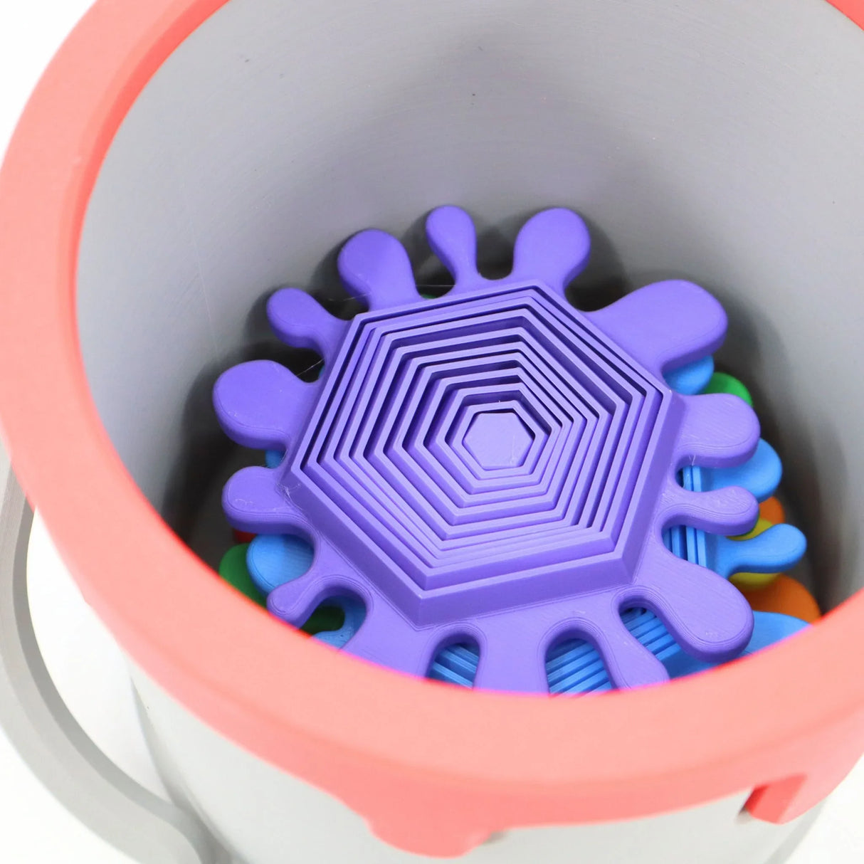 Colorful 3D printed sensory toy with hexagonal and splatter shapes inside a round container