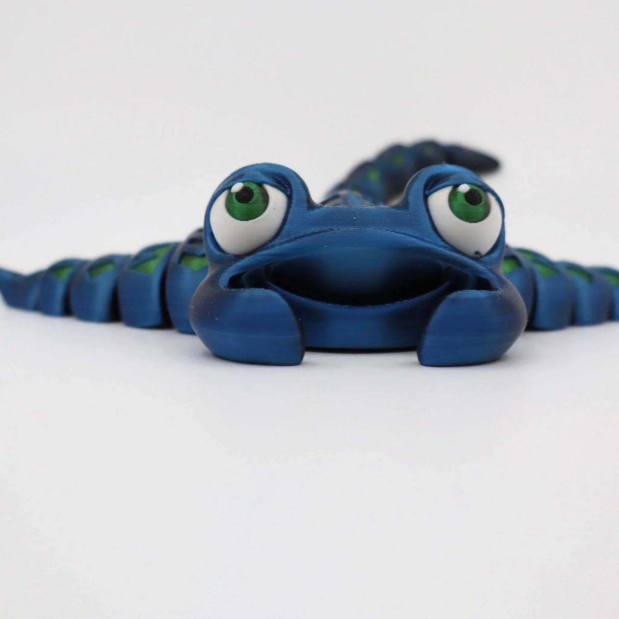 Blue 3D printed sensory toy lizard with green eyes on white background
