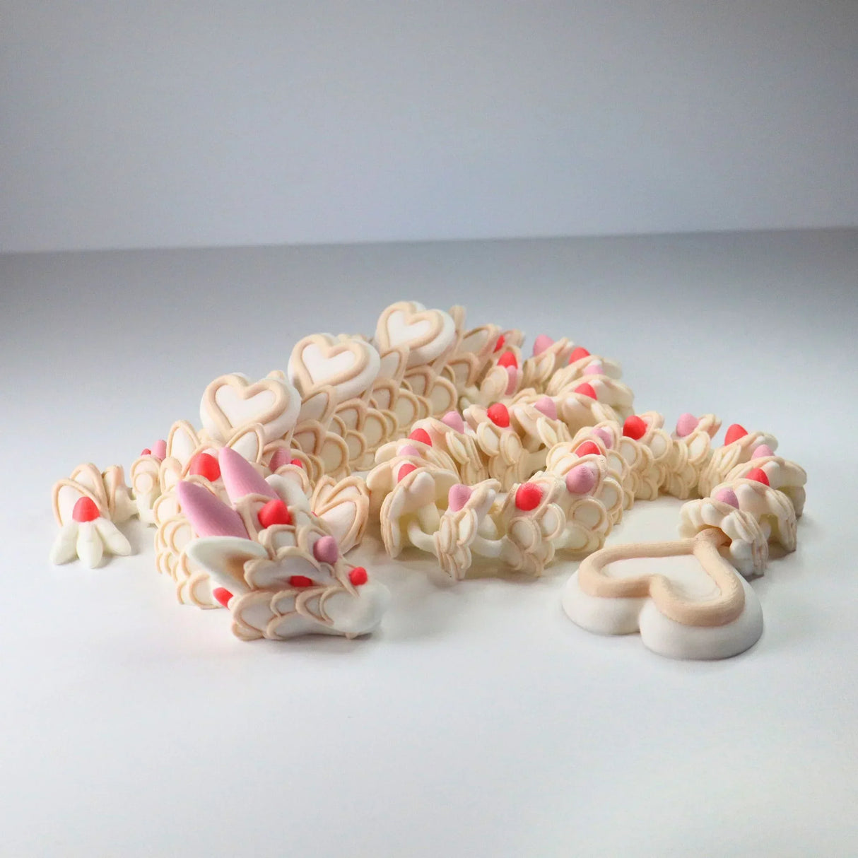 3D printed sensory dragon toy with heart-shaped scales, cream and pink colors, on white background