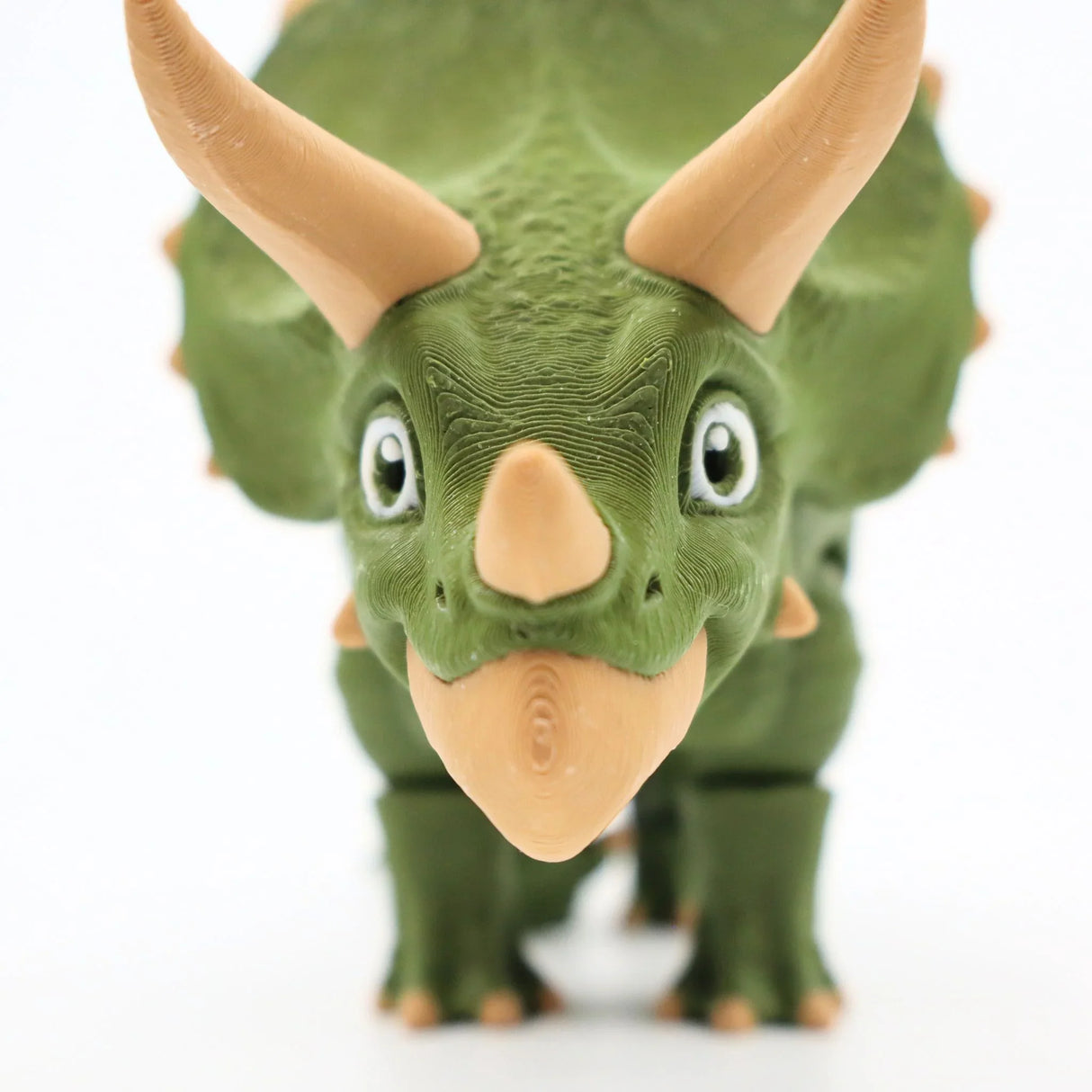 3D printed green triceratops sensory toy with tan horns and textured surface on white background
