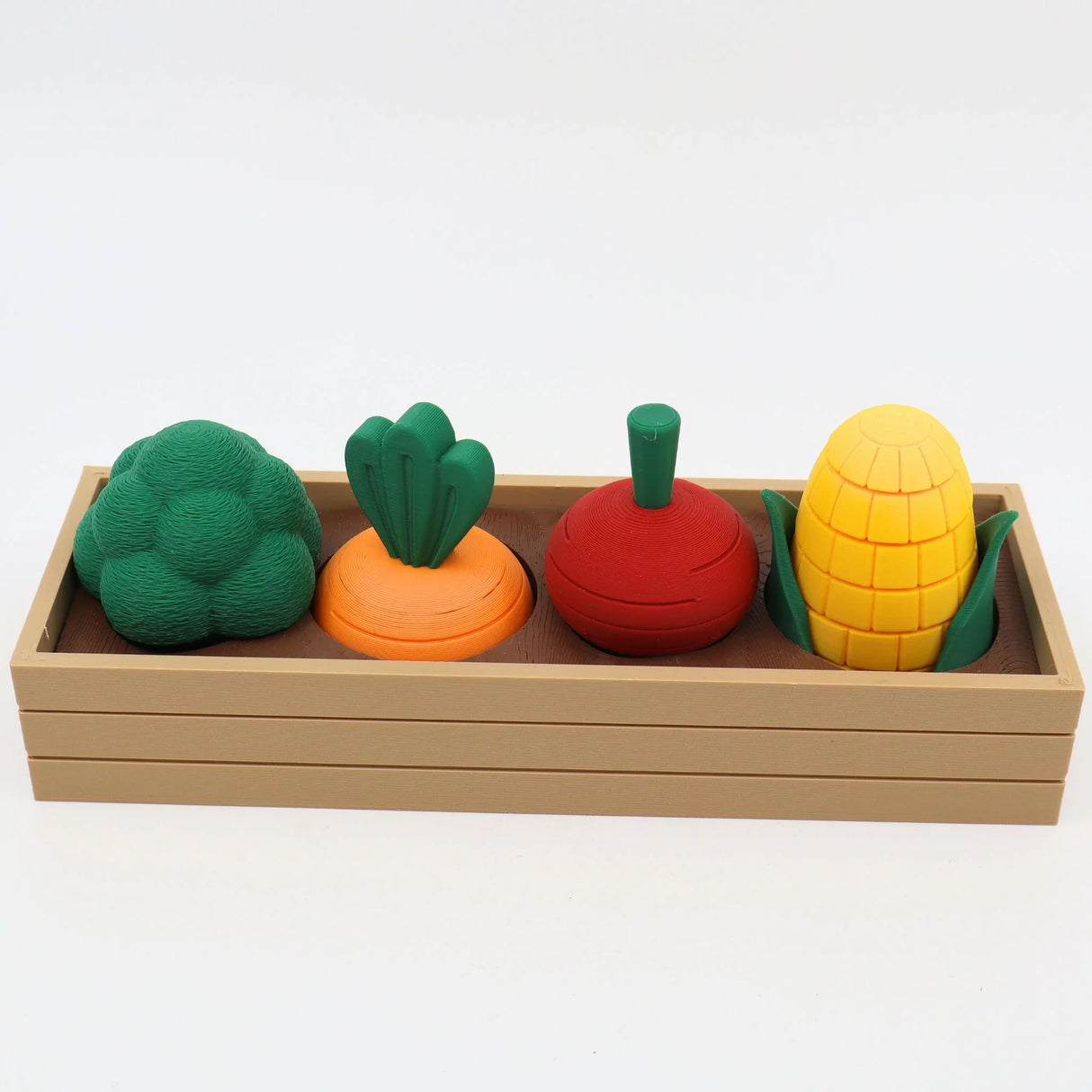 Colorful 3D printed sensory vegetable toys in a wooden tray, including broccoli, carrot, tomato, and corn