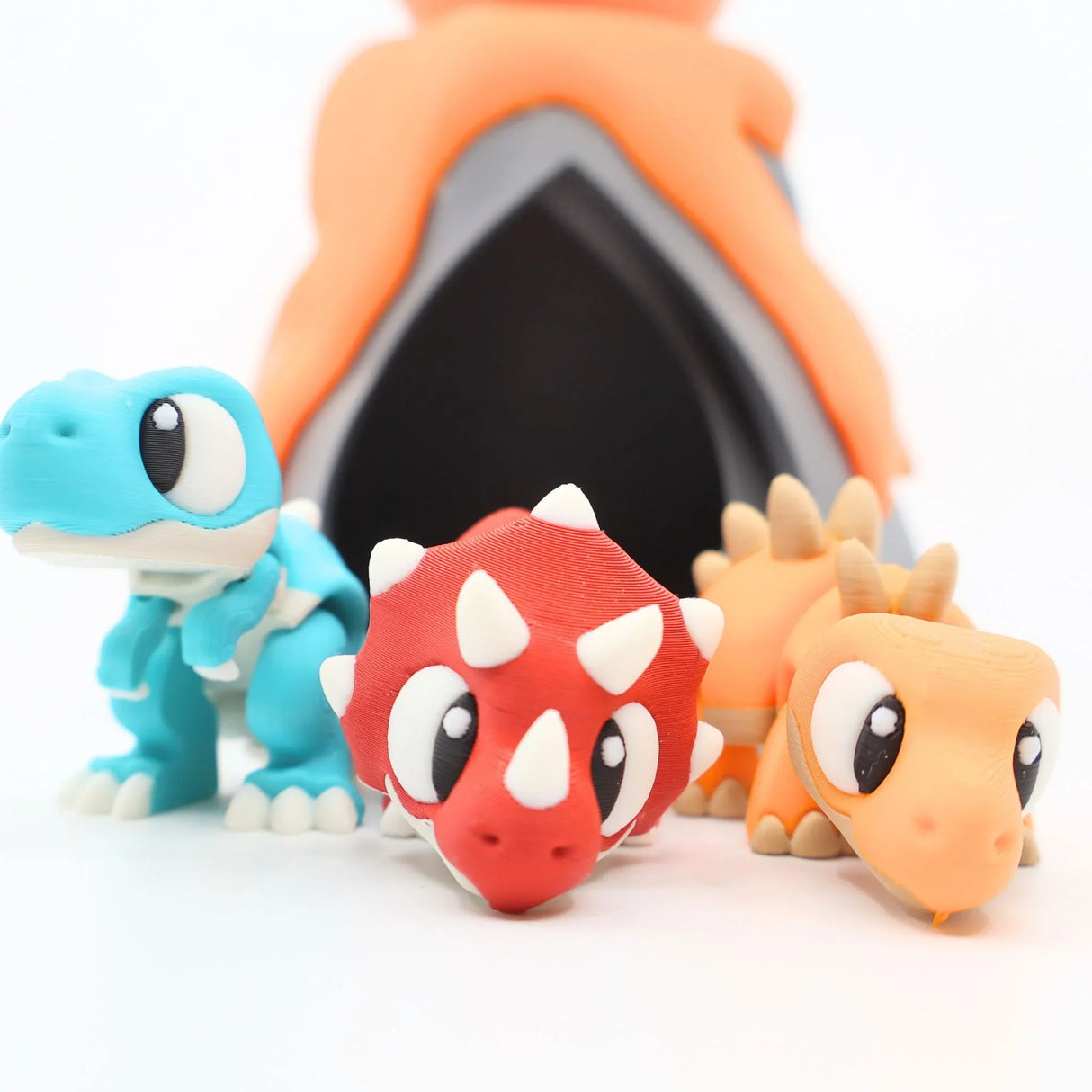 Three colorful 3D printed dinosaur sensory toys in front of a toy volcano