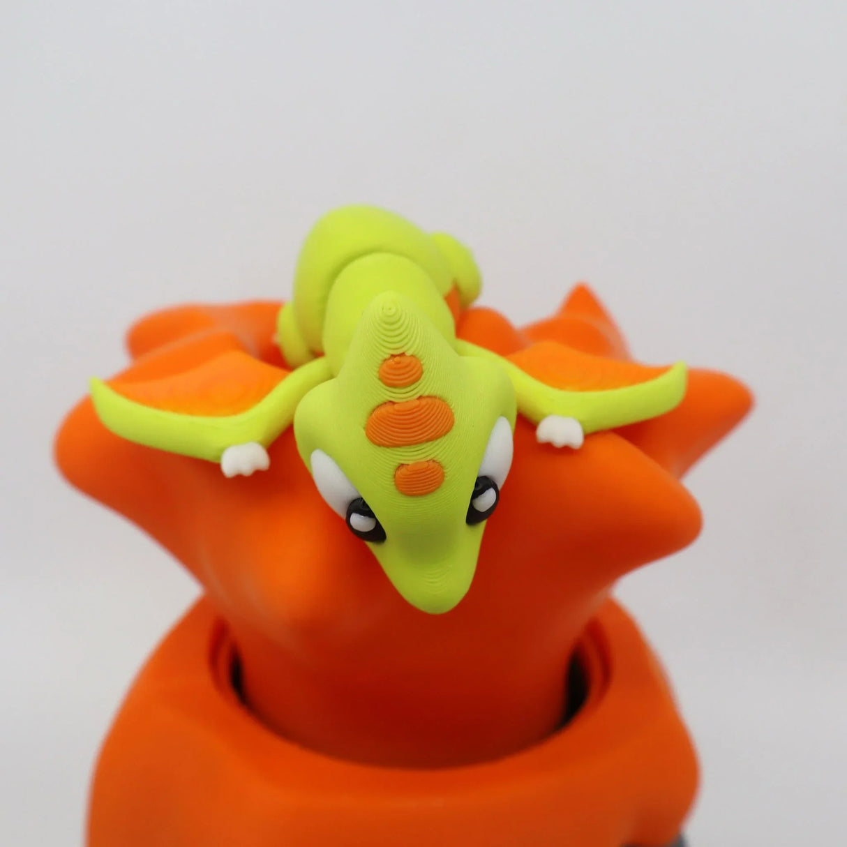 3D printed green and orange dragon toy sitting on a bright orange volcano