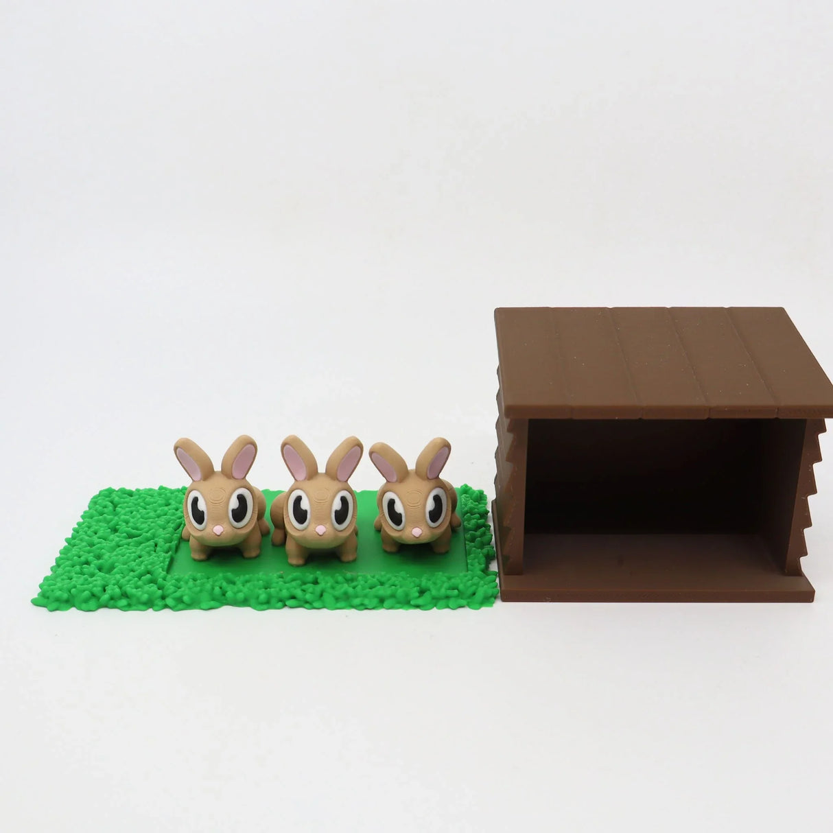 Three cute 3D printed bunny toys on green mat beside brown hutch, sensory educational toy