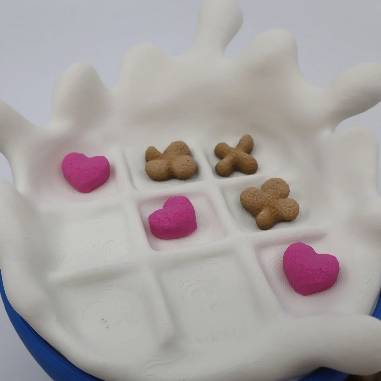 3D printed sensory tic-tac-toe game with heart and X pieces on a white splash-shaped board