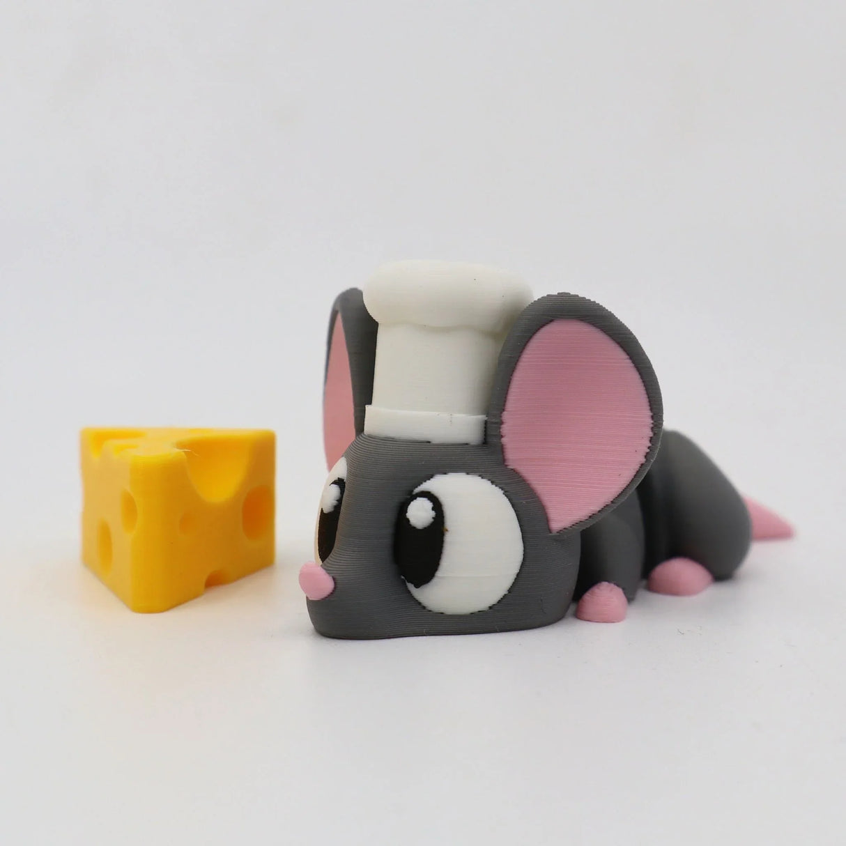 3D printed gray mouse figurine with chef hat and pink ears beside a yellow cheese block toy