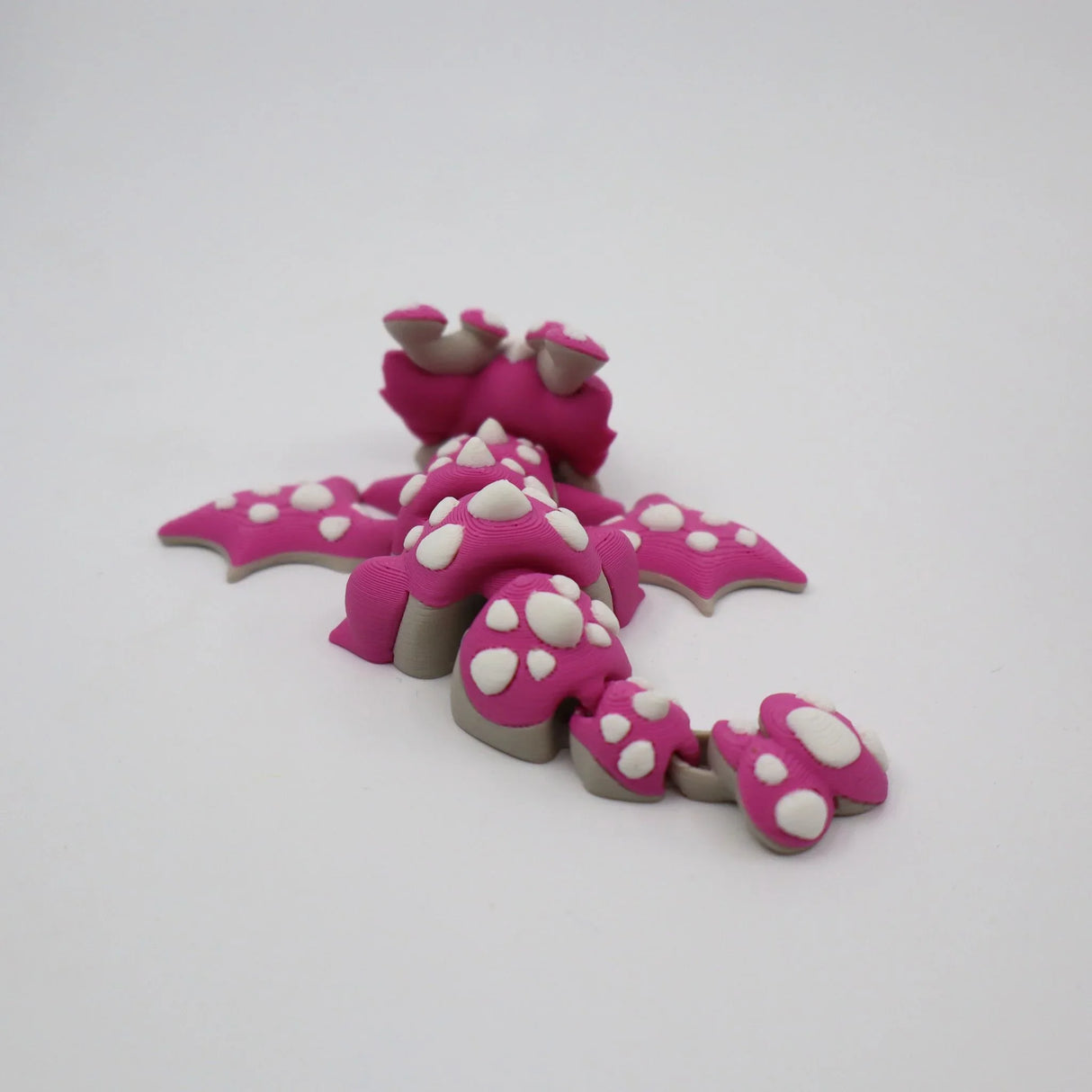 Pink 3D printed flexi dragon fidget toy with white spikes, designed for sensory play and tactile stimulation.