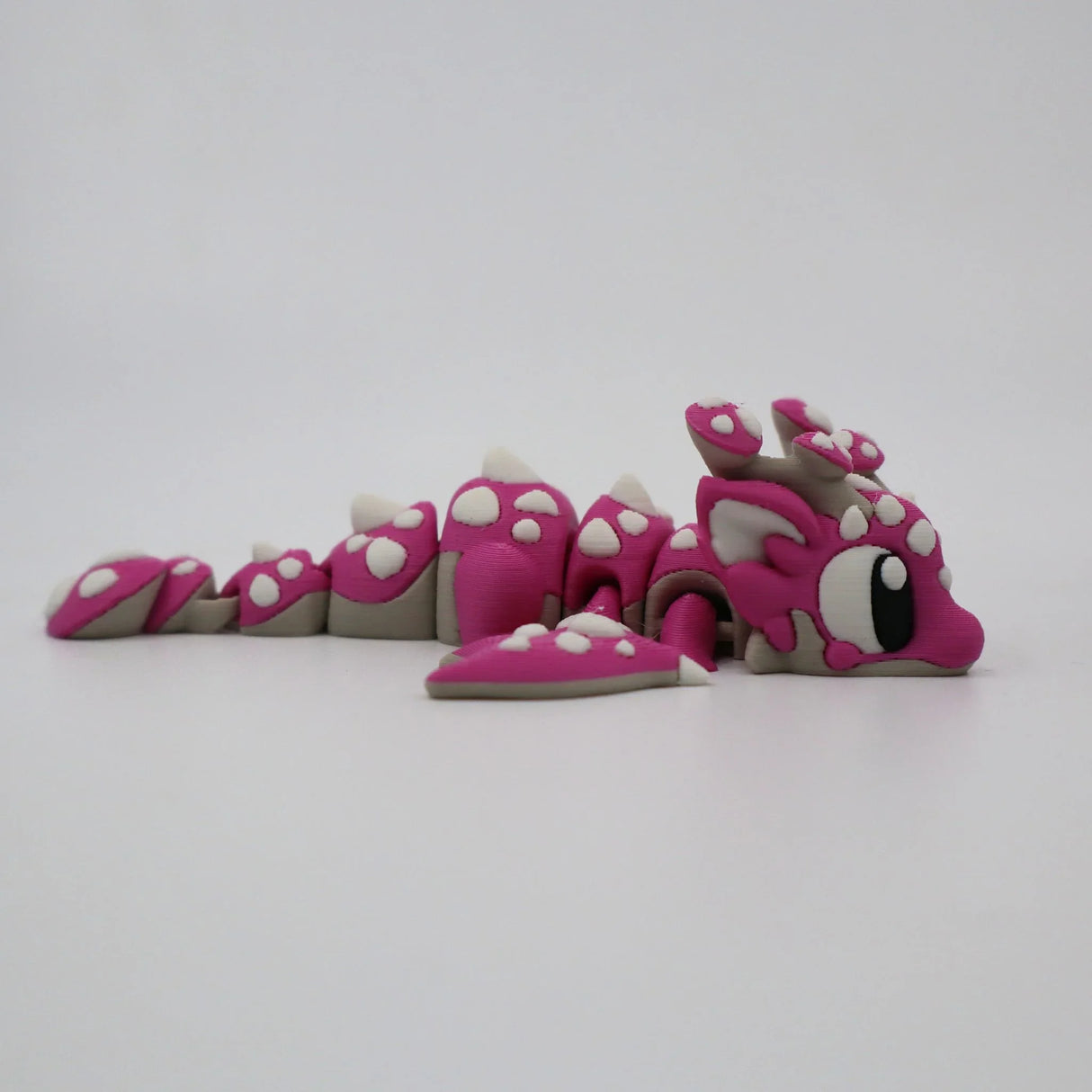 Pink 3D printed flexi dragon fidget toy with white spots, designed for sensory play and tactile stimulation