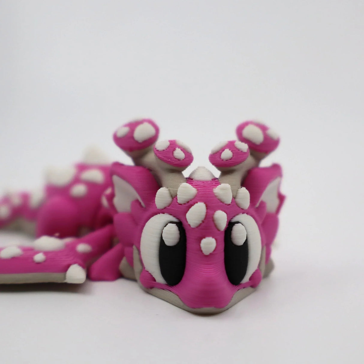 Pink 3D printed flexi dragon fidget toy with white spikes and big eyes for sensory play