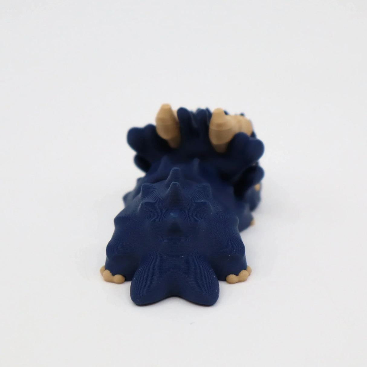 Blue 3D printed sensory dinosaur toy with beige horns on a white background