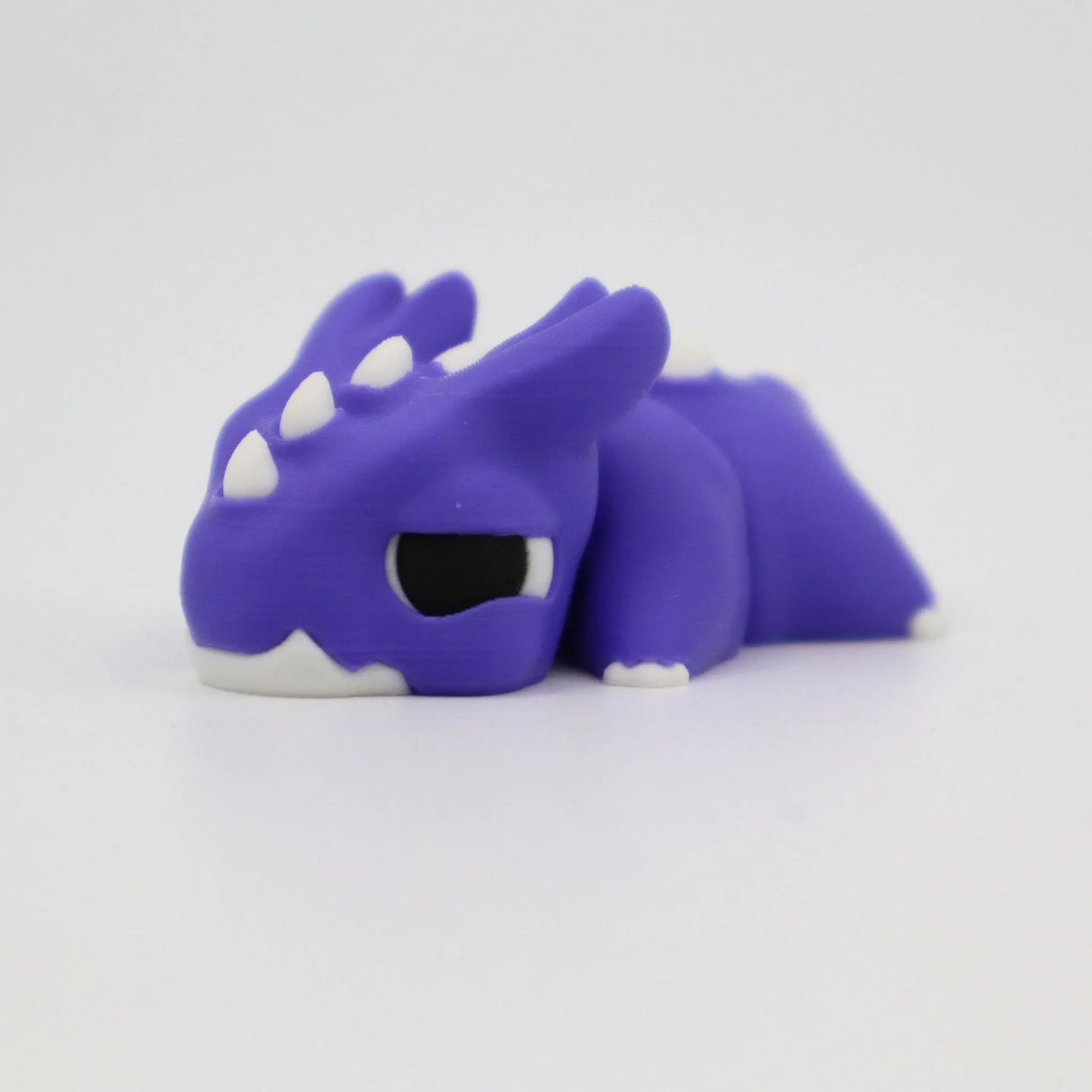 Purple 3D printed sensory dragon toy with white horns and black eyes on white background.