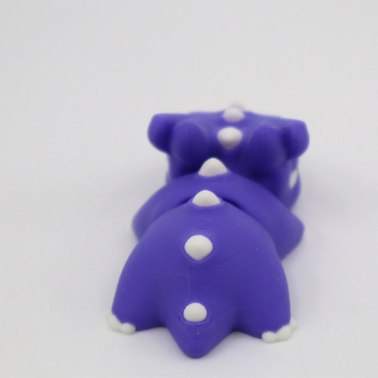 Purple 3D printed dinosaur sensory toy with white spikes on a white background