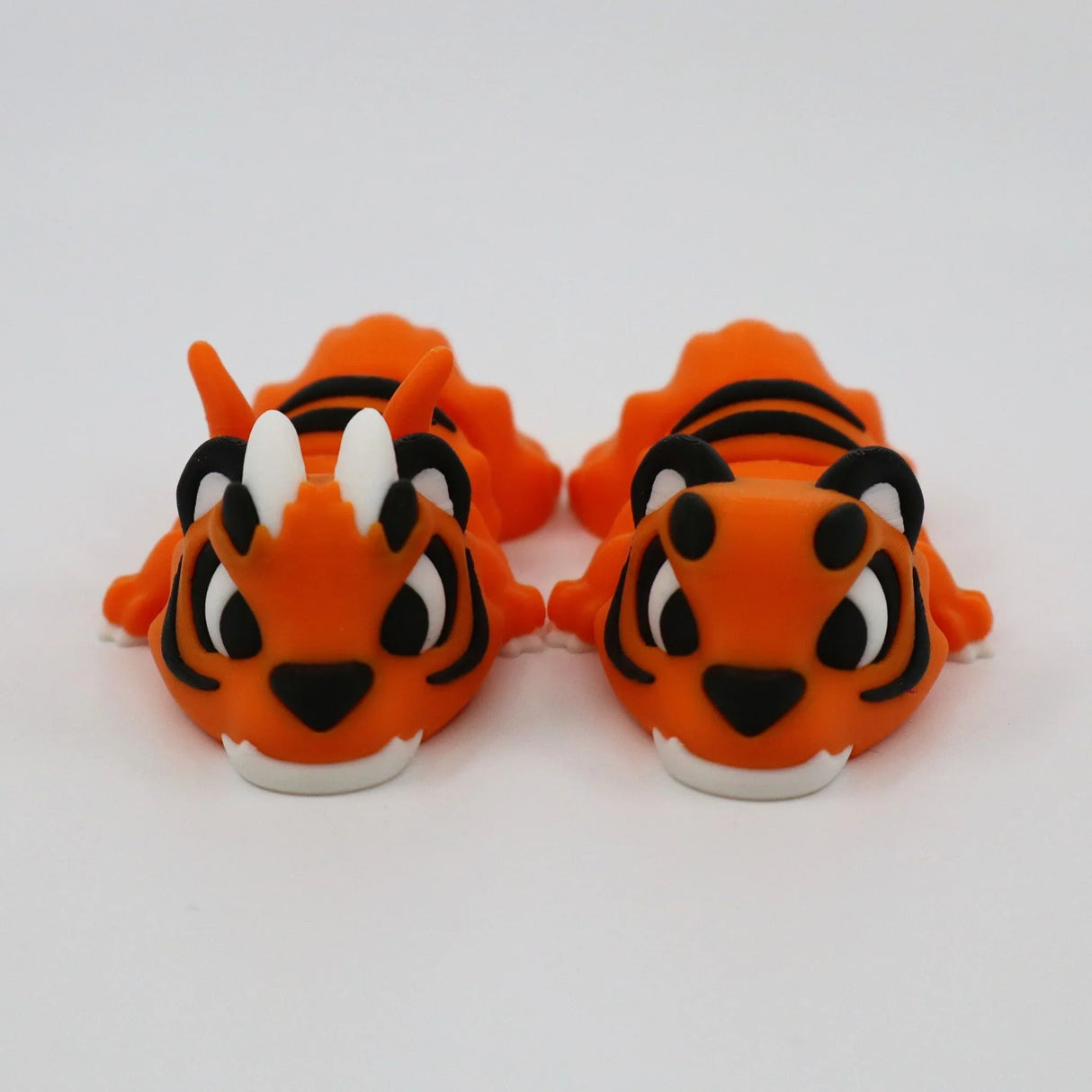 Pair of orange 3D printed sensory tiger toys with black stripes on a white background