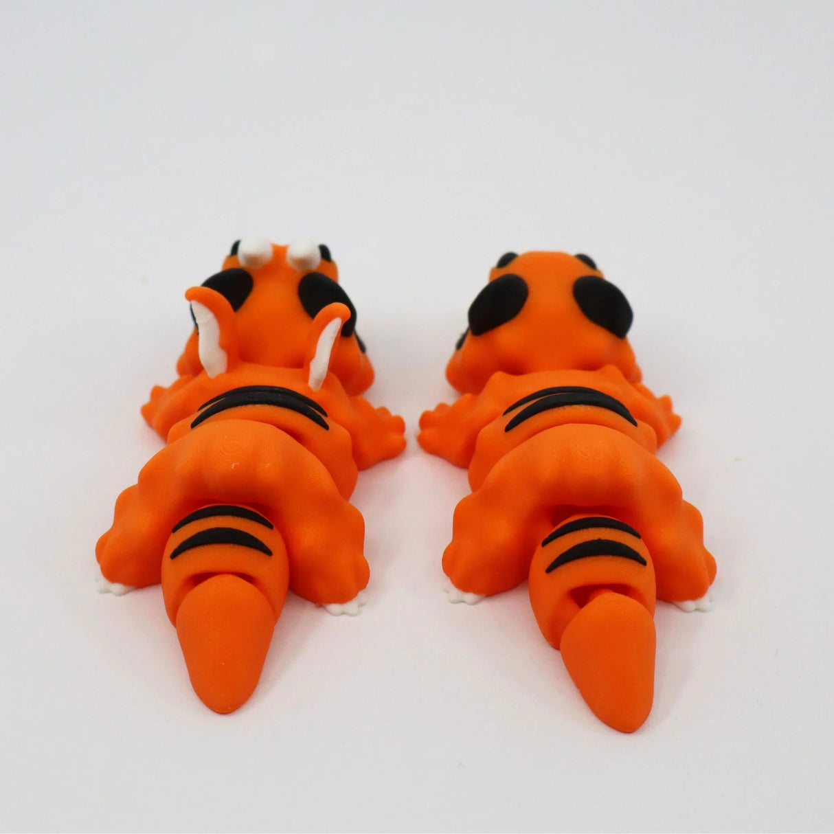Two orange 3D printed sensory tiger toys with black stripes, viewed from behind