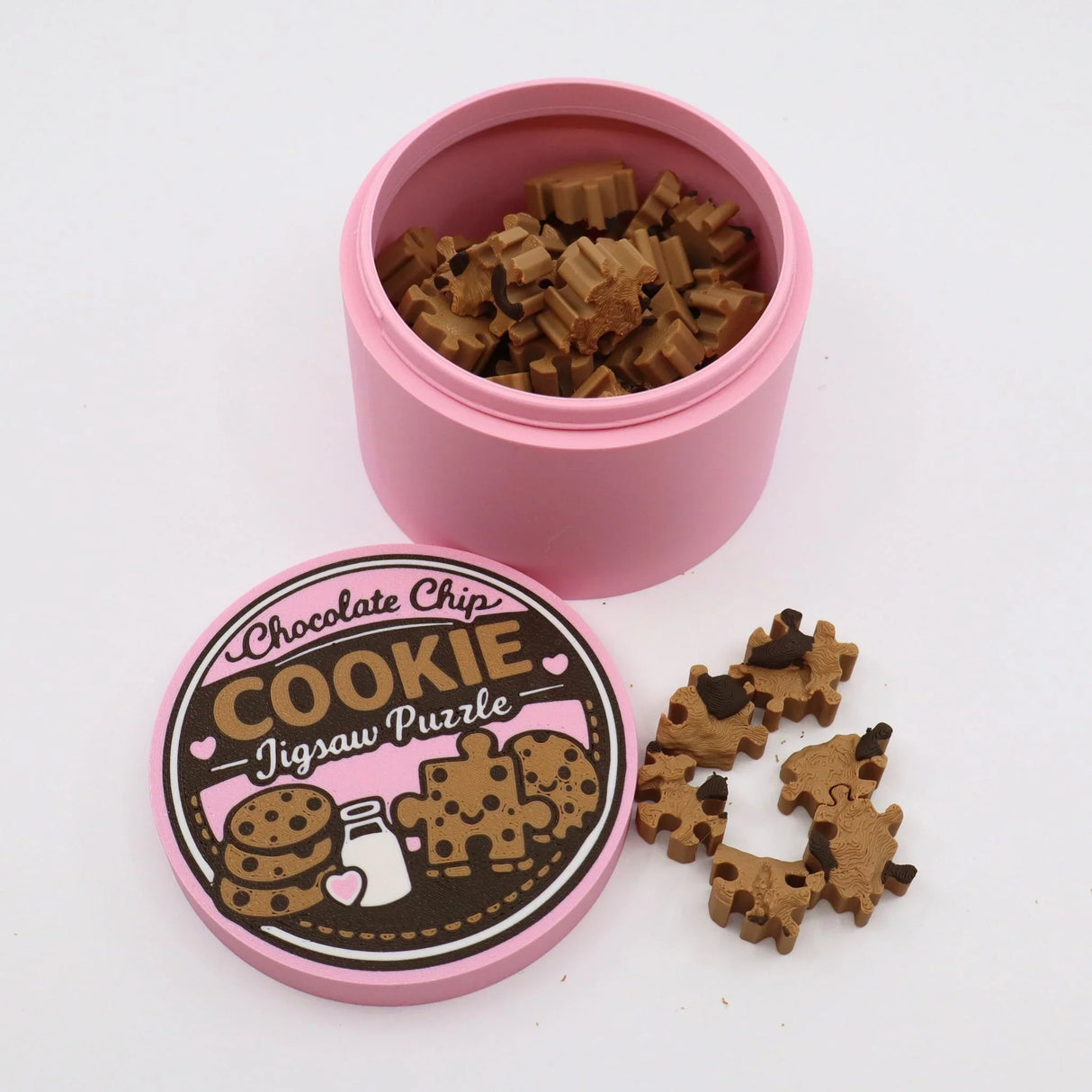 Chocolate chip cookie jigsaw puzzle pieces in a pink container with illustrated lid.