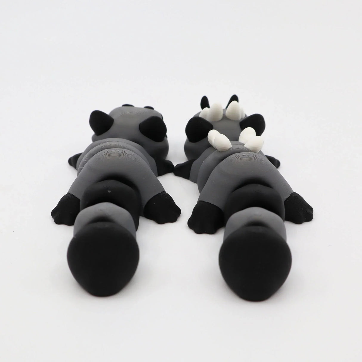 Two gray and black 3D printed sensory animal toys lying side by side on a white background.