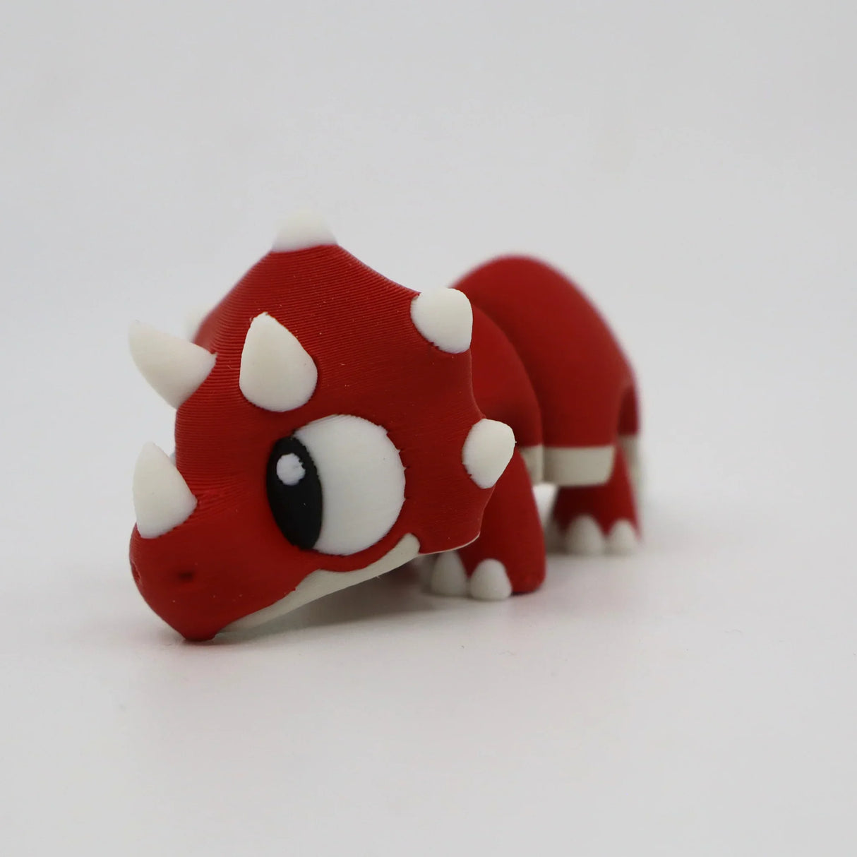Red 3D printed triceratops sensory toy with white horns and cute cartoon eyes
