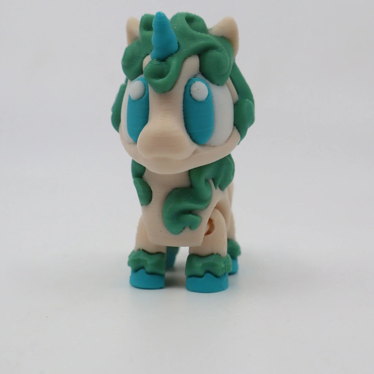 3D printed unicorn sensory toy with blue horn, green mane, and large blue eyes