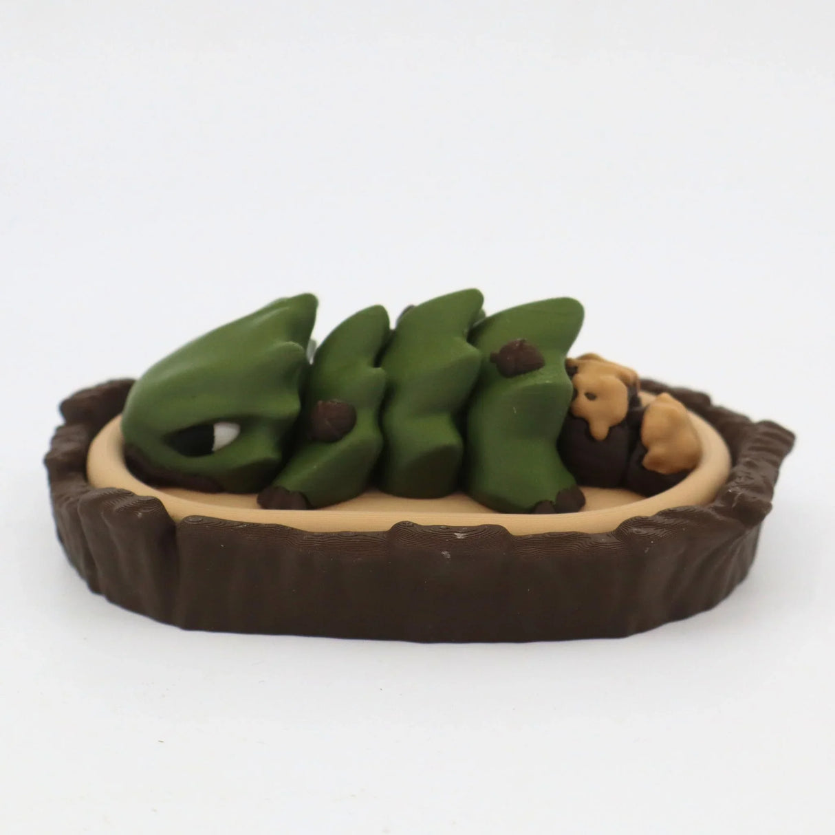 Green 3D printed dinosaur toy curled up in a nest with two small brown animals