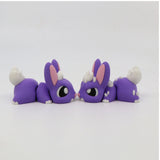 Two purple 3D printed bunny sensory toys with white tails and pink ears facing each other