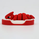 Red 3D printed sensory toy in the shape of a curled creature on a white base