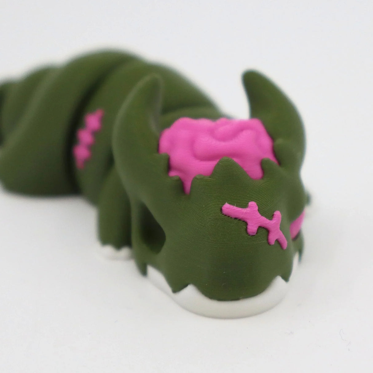 Green 3D printed sensory toy caterpillar with pink brain detail and stitches, on white background