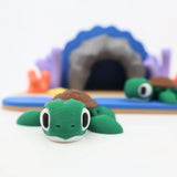 3D printed green turtle sensory toy on beach playset with cave and coral decorations