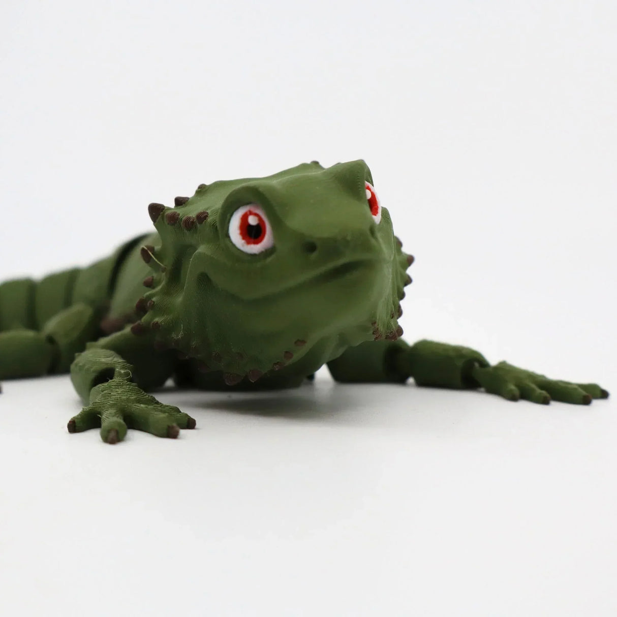 3D printed green bearded dragon sensory toy with red eyes on white background