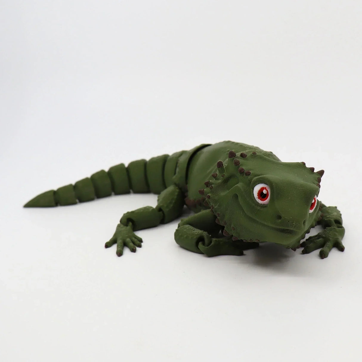 Green 3D printed sensory lizard toy with red eyes on a white background