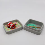 Colorful 3D printed ladybug sensory toy in a gray box with flower and leaf decorations.
