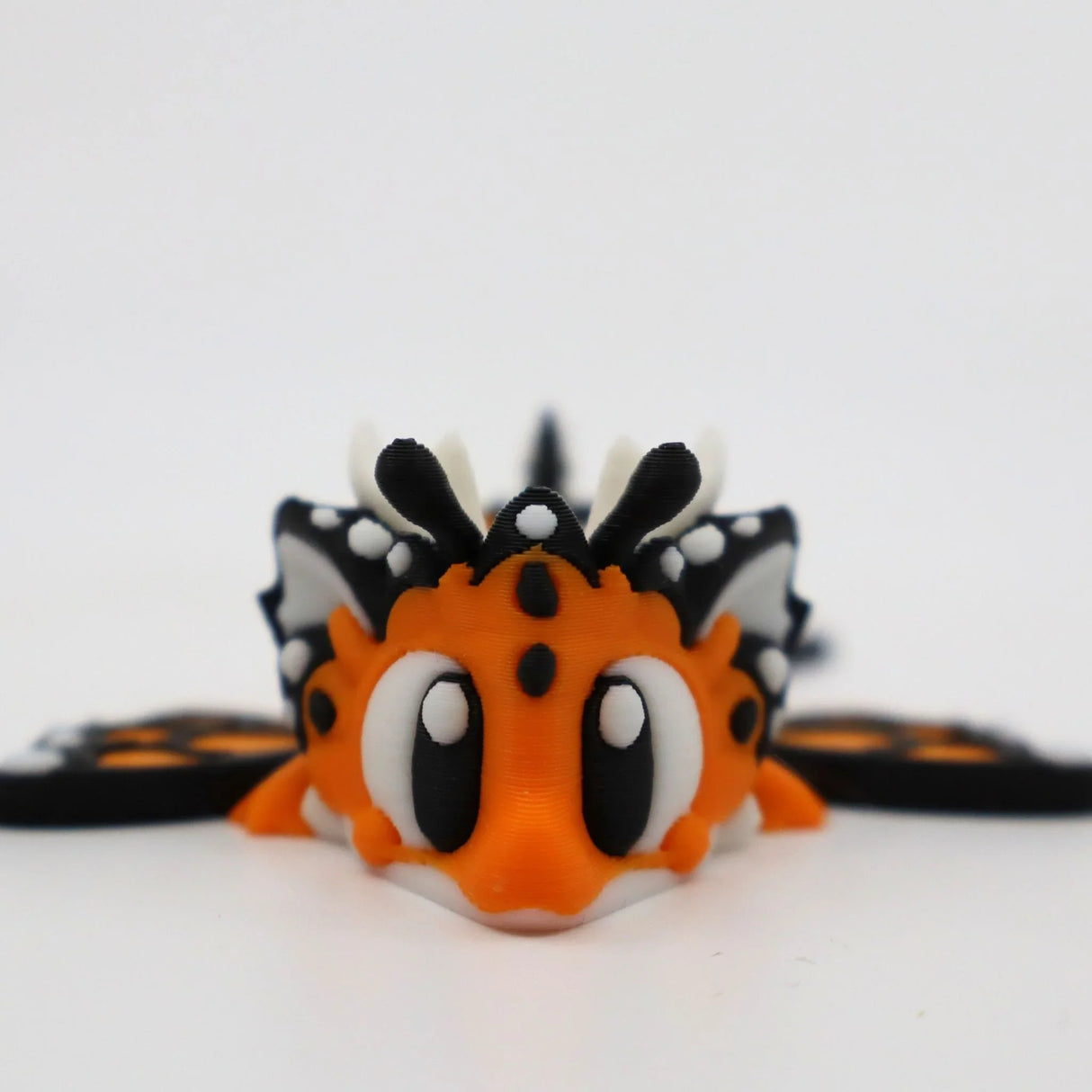 Cute orange and black 3D printed butterfly sensory toy with big eyes on a white background