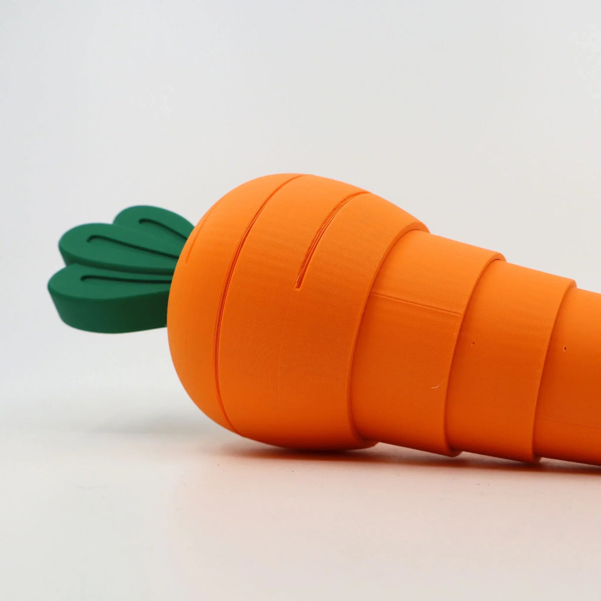 3D printed orange carrot-shaped sensory fidget toy with green leaves on white background