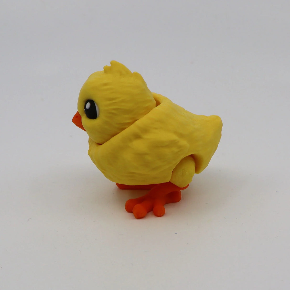 Yellow 3D printed sensory toy chick with orange feet and big black eyes on white background.