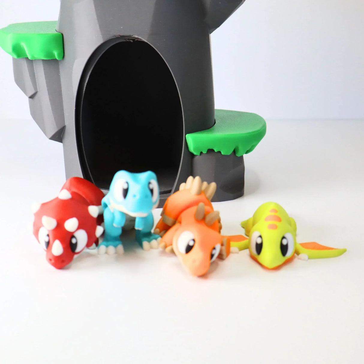 Colorful 3D printed dinosaur sensory toys in front of a toy cave