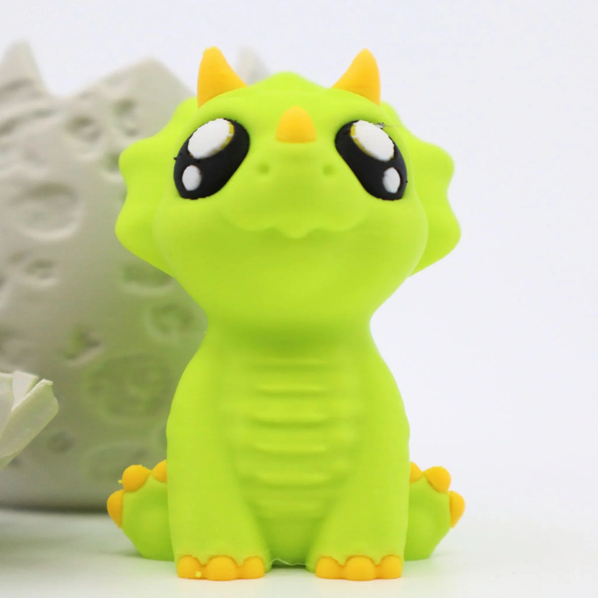 Cute green dinosaur fidget toy with big eyes, yellow horns, and sensory details
