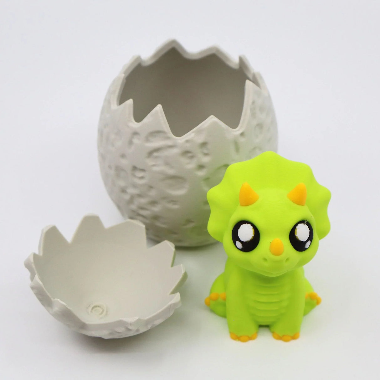Cute green triceratops sensory toy with 3D printed dinosaur egg shell on white background