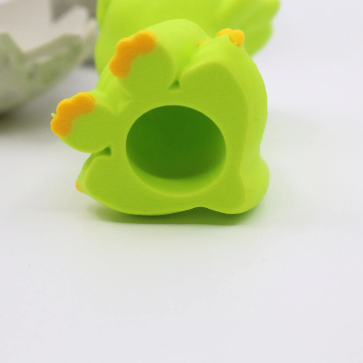 Green 3D printed dinosaur finger fidget toy with yellow claw details on a white background