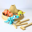 Colorful 3D printed dinosaur sensory toys in a mini sandbox with volcano and toy tools
